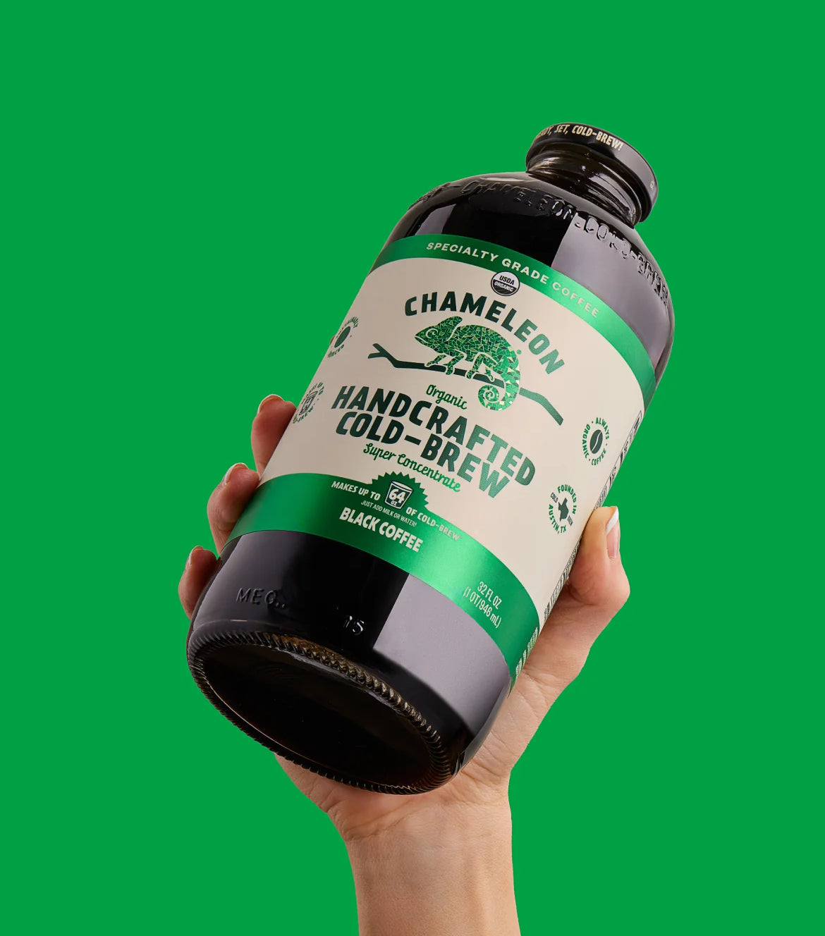 A hand holding a bottle of Chameleon organic cold brew concentrate against a green background.